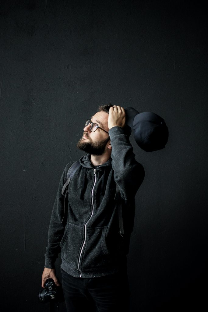 Bearded man with glasses, holding cap with hand on head looking up. Noticing where you are and what's around you helps with movement and balance.