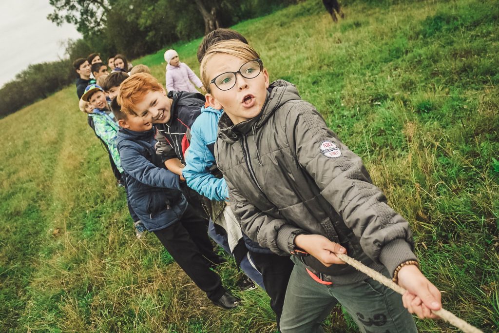 Group of boys and girls pulling on one end of a thick rope in a tug of war.