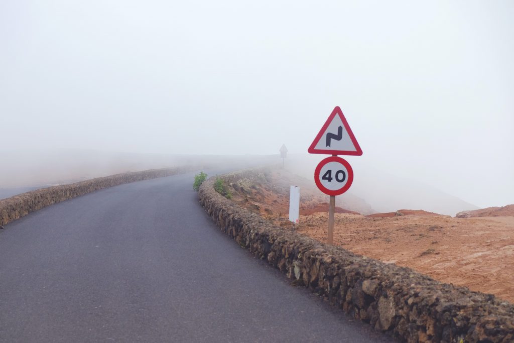 Winding country road disappearing into the fog with a speed limit sign of 40 kmp (25 mph). Staying within limits can keep you safe.
