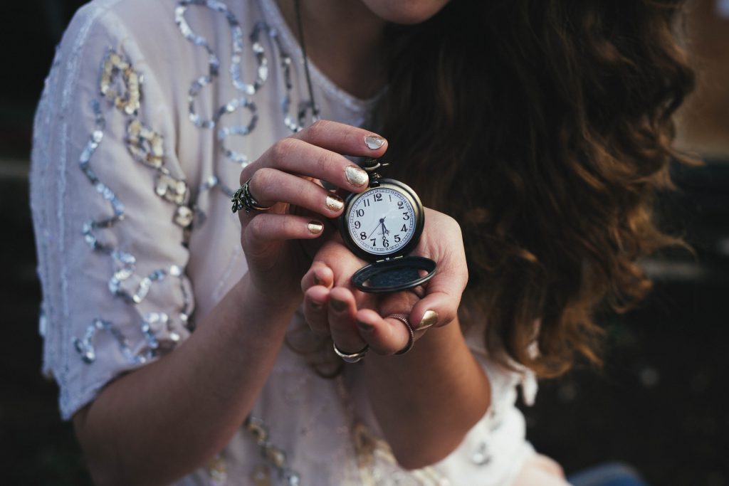Woman holding open antique pocket watch up in both hands to show the time.