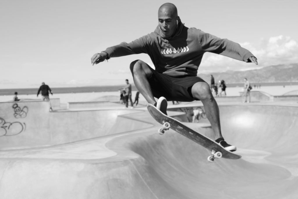 Young man doing a tricky move on his skateboard in a skateboard park with lots of slopes, ridges, and features requiring serious attention and concentration.