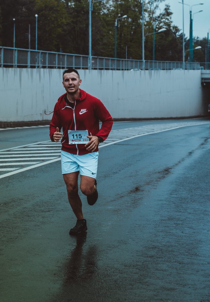 Middle aged man running in a competition wearing a red sweatshirt with his entry number and white shorts.