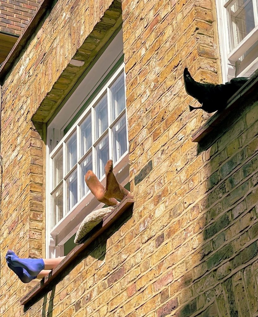 Ankles and feet sticking out of apartment windows. One barefoot, one with blue socks, and one with black boots with spike heels.