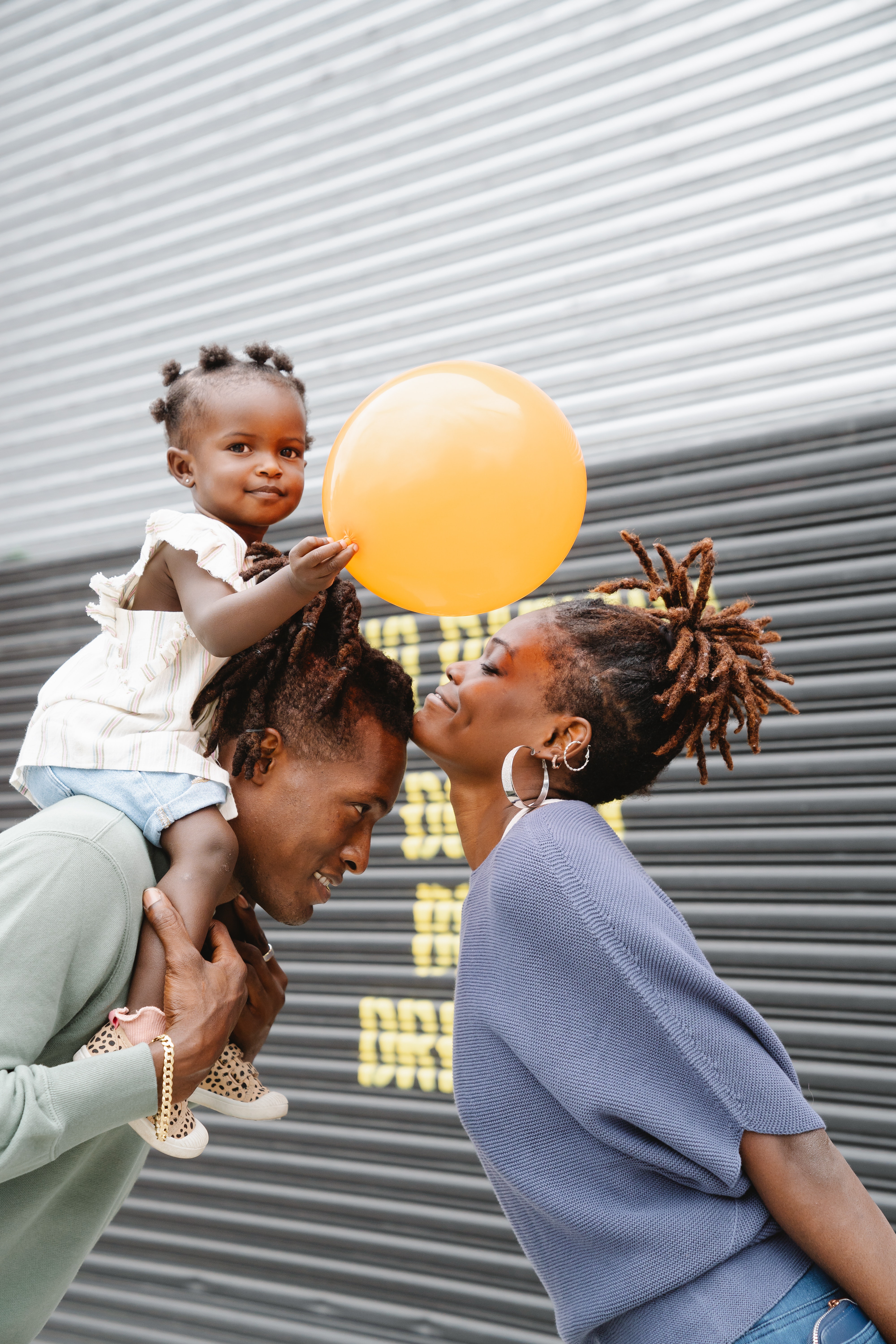 Toddler with orange balloon on father's shoulders, mother and father bending toward each other.
