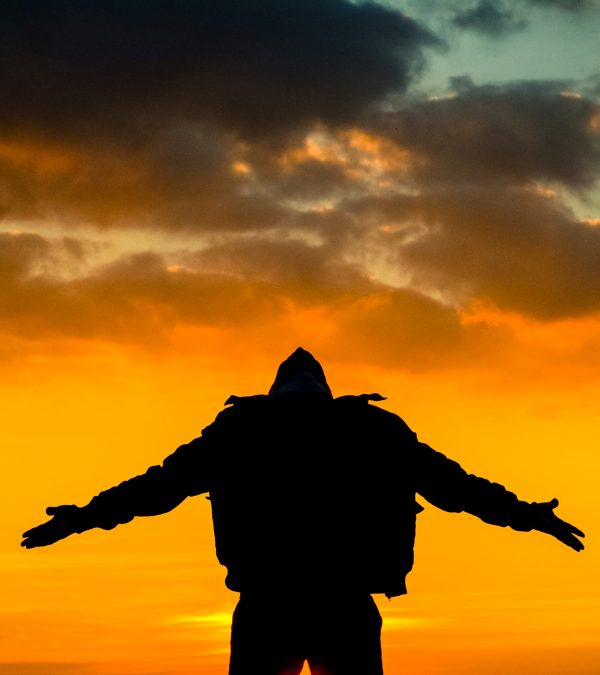 Man silhouetted in the sunset with his arms outspread and head flung back.